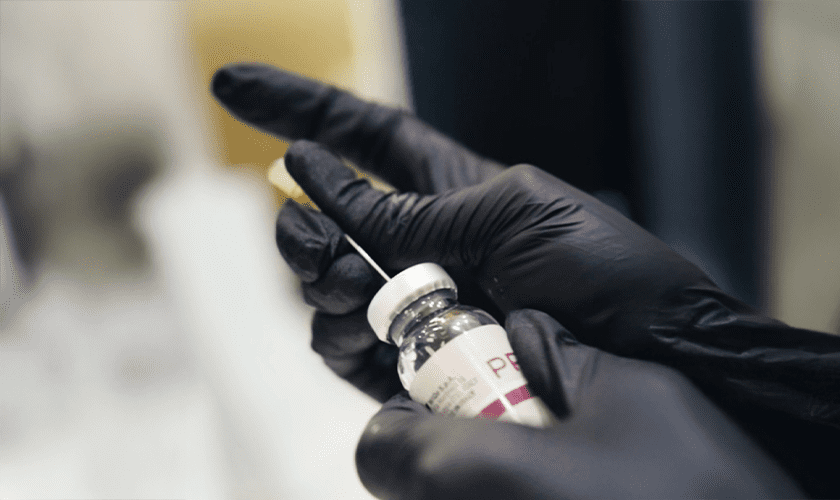 A person wearing black gloves inserts a needle into a vial, preparing to draw liquid from the bottle—suggesting a clinical atmosphere typical of medycyna estetyczna Wrocław or procedures like powiększanie ust Wrocław.