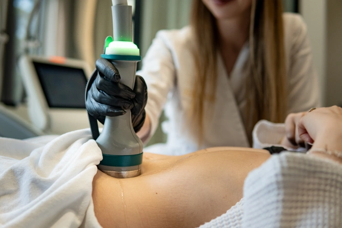 Klinicysta w czarnych rękawiczkach wykonuje nieinwazyjny zabieg modelowania sylwetki za pomocą ręcznego urządzenia na odsłoniętym brzuchu osoby w klinice medycyny estetycznej we Wrocławiu lub w spa.