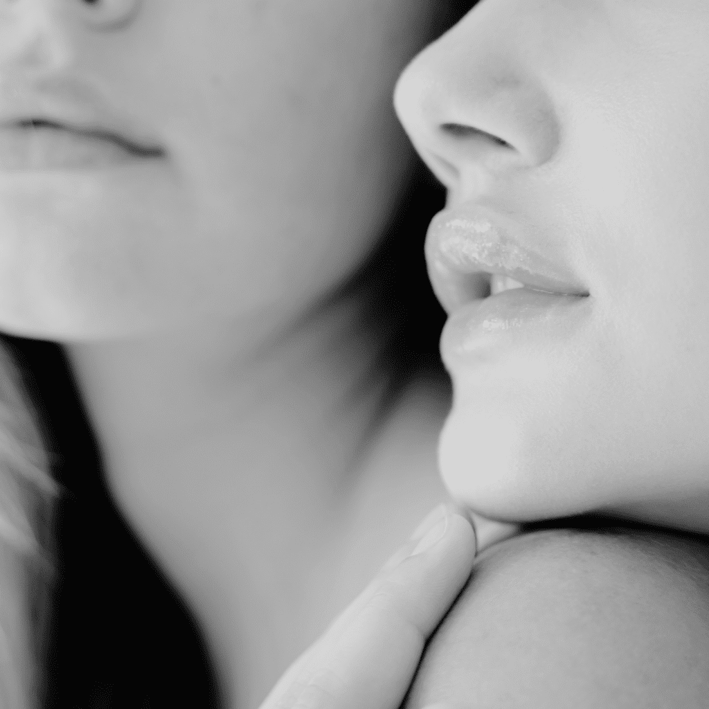 Close-up black and white photo of two people, focusing on their lips and chins. One person’s hand gently touches the other’s face, creating an intimate atmosphere—an elegant moment reminiscent of medycyna estetyczna Wrocław.