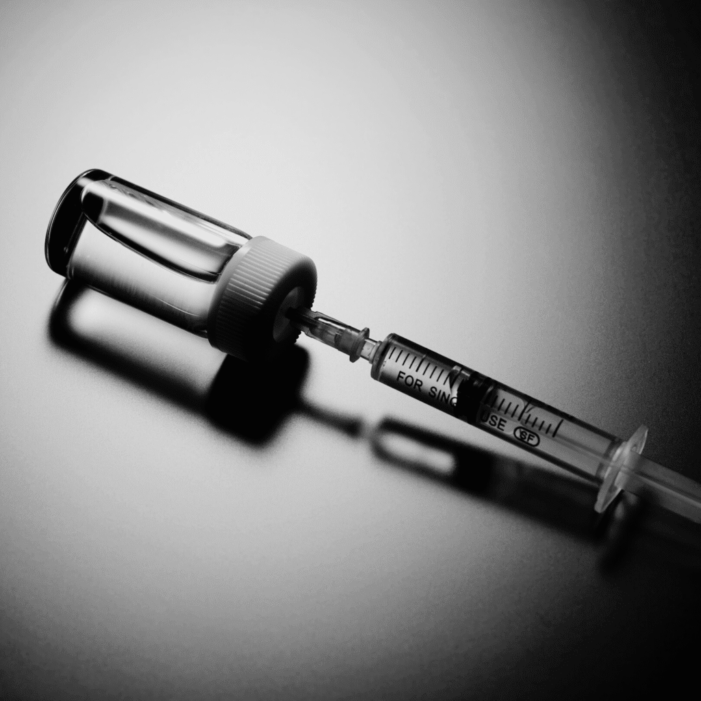 A syringe draws liquid from a glass vial against a dark, reflective surface, suggesting a medical or vaccination theme—ideal for illustrating procedures at a klinika medycyny estetycznej or powiększanie ust Wrocław.